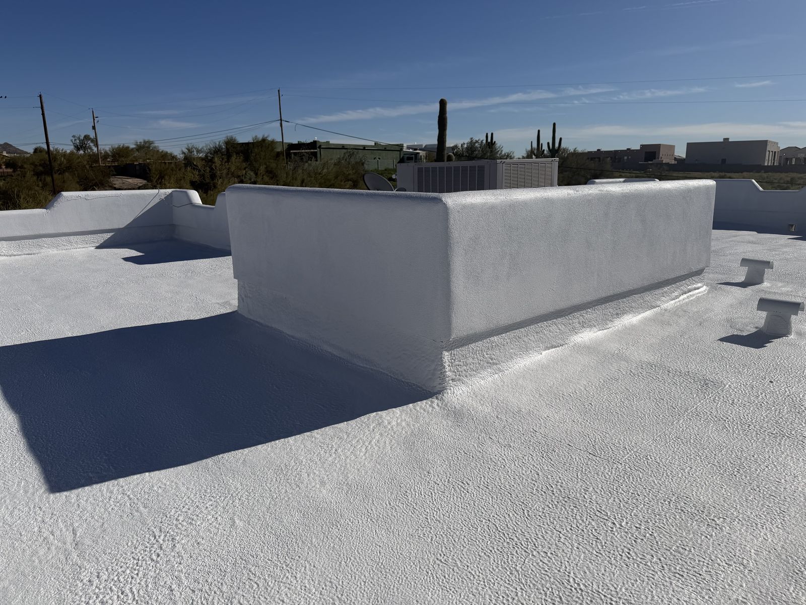 Finished white flat-roof coating meeting a parapet wall