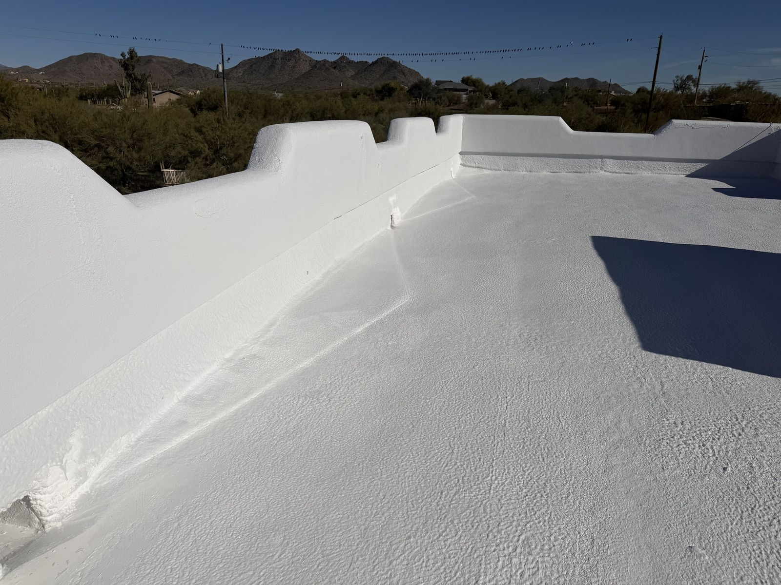 The same flat roof recoated in white, parapet and roof deck sealed, desert mountains behind
