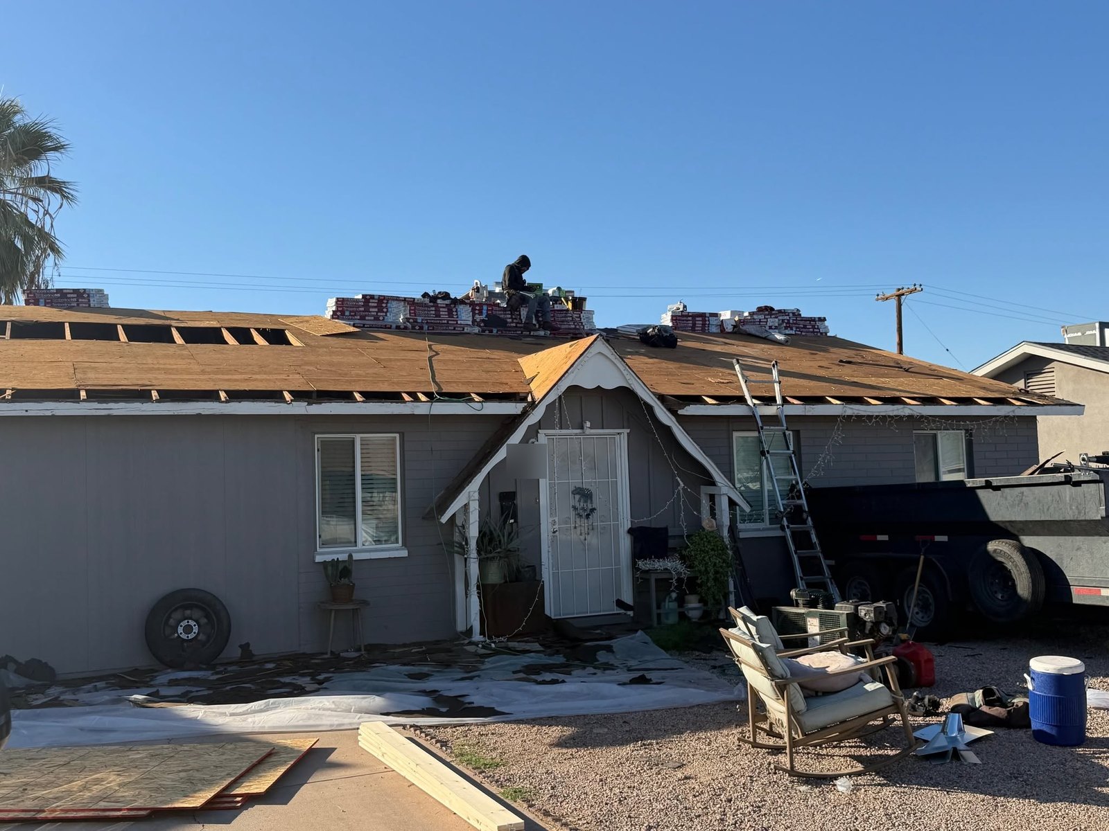 Tear-off in progress from the street, decking going down and bundles staged on the roof